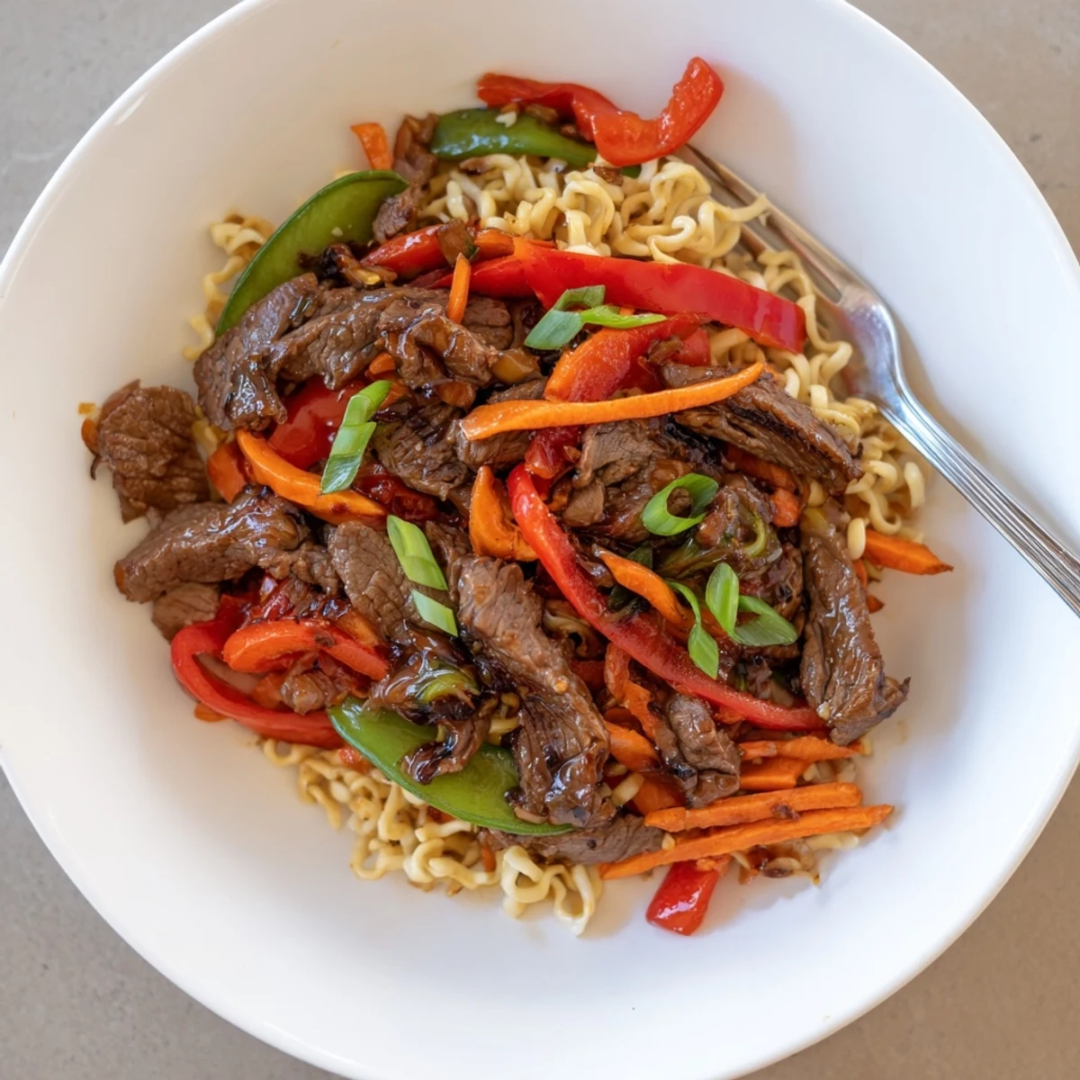 A close-up of a flavorful Teriyaki Beef & Noodle Bowl with visible vegetables and tender beef strips.