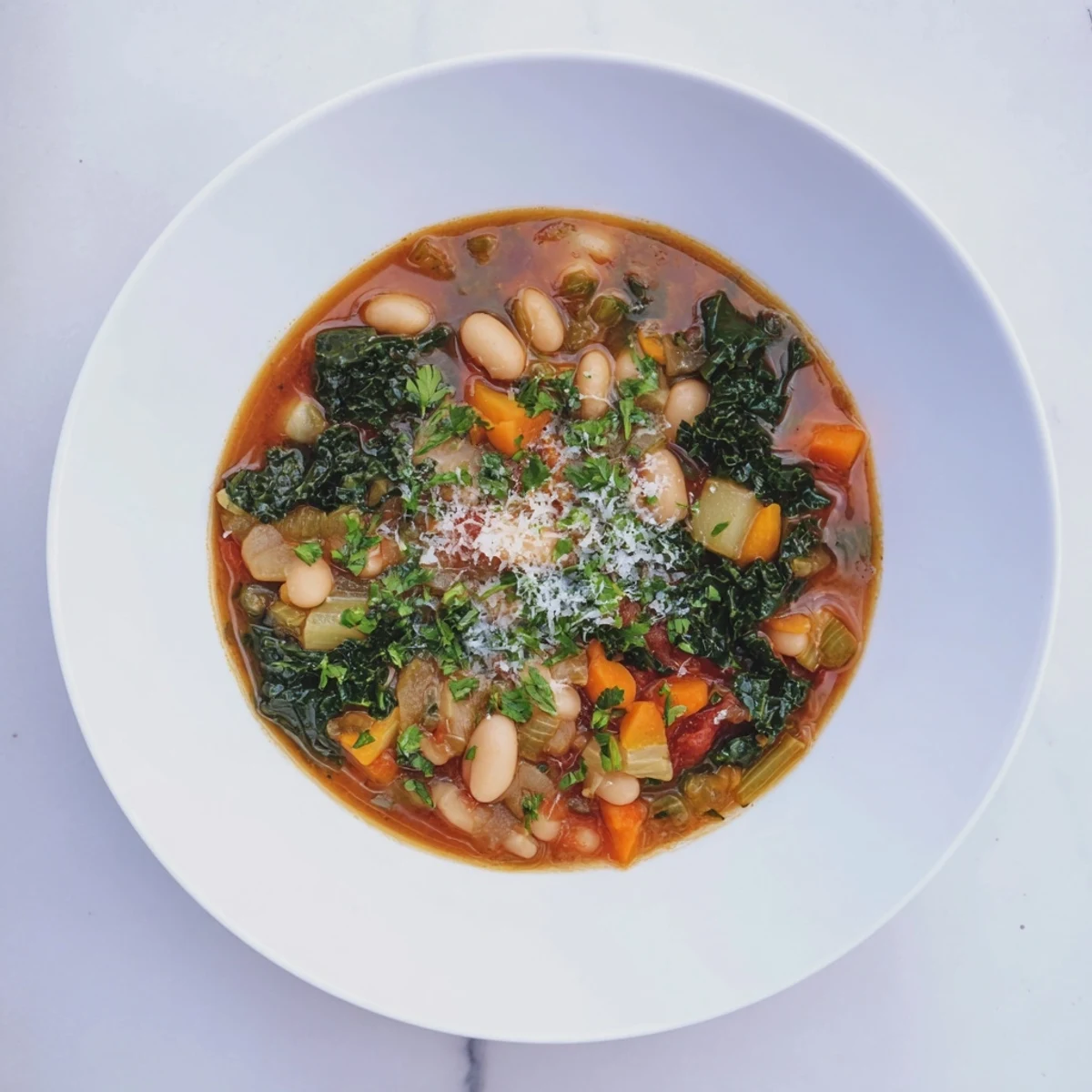 A close-up of the delicious Italian Bean & Kale Stew, garnished with fresh herbs and Parmesan.