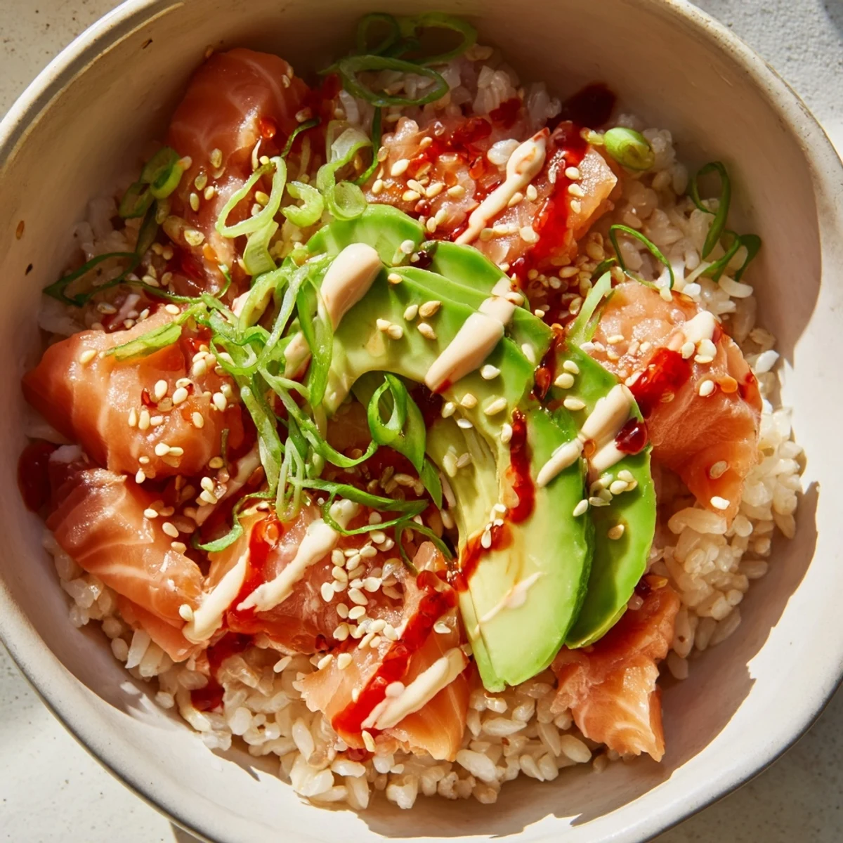 This Emily Mariko salmon rice bowl features glistening rice, spicy mayo, and toasted sesame seeds ready to eat.