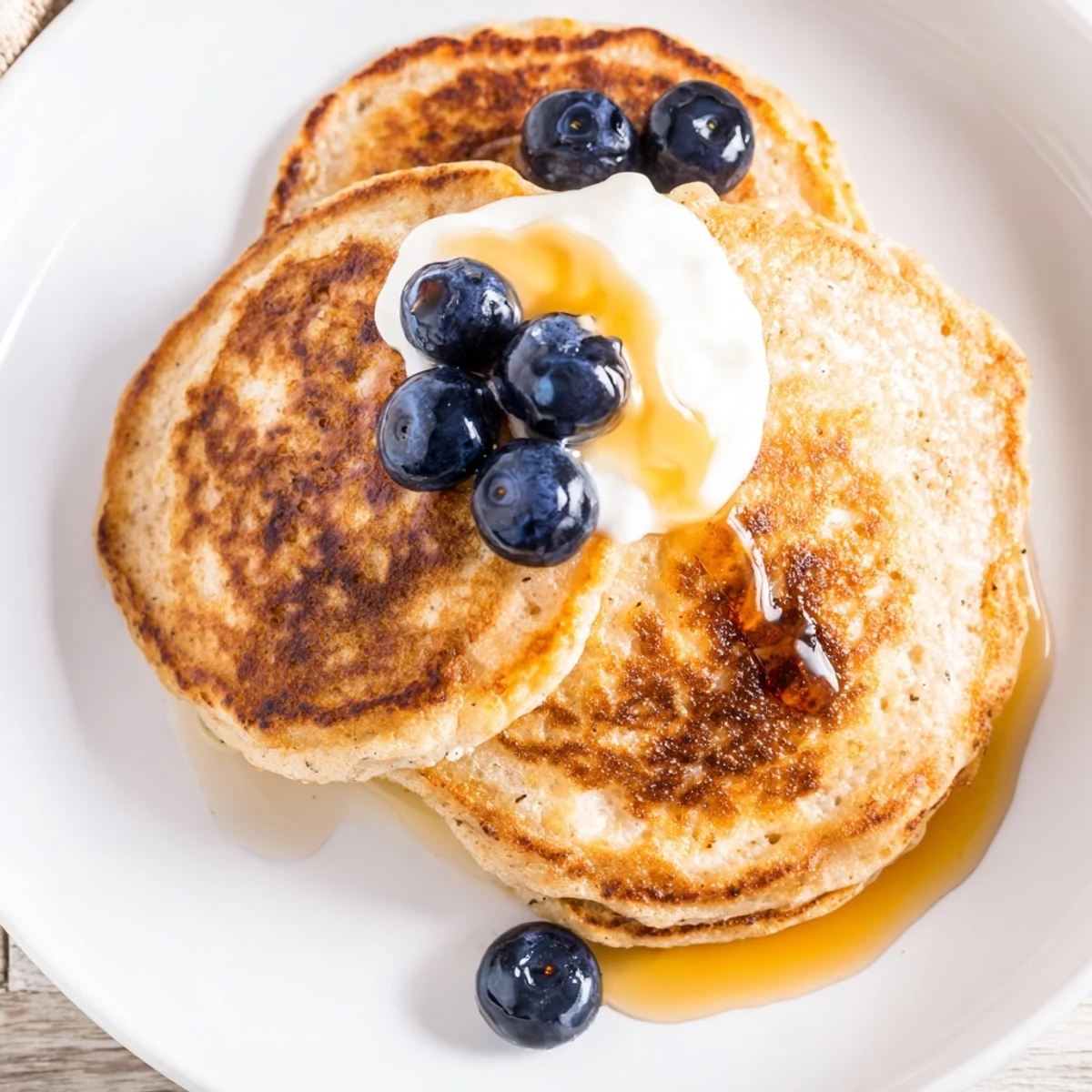 A plate of freshly cooked cottage cheese pancakes, drizzled with sweet maple syrup and topped with berries.