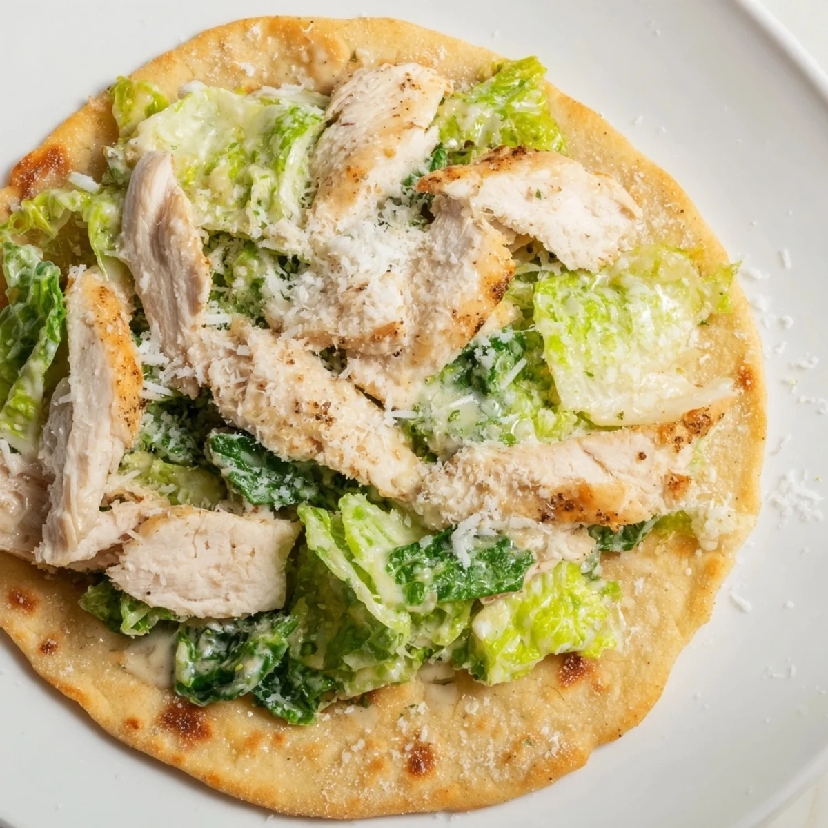 A close-up of Chicken Caesar Flatbread showing crispy golden crust, grilled chicken slices, fresh romaine, and a drizzle of creamy Caesar dressing.  