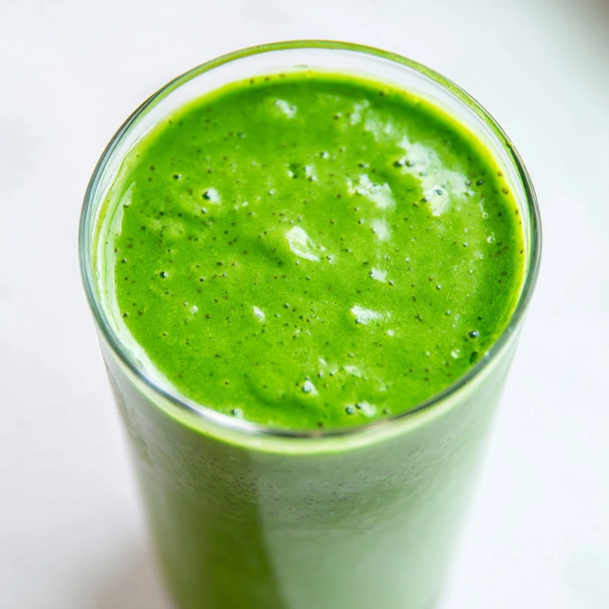 The Green Detox Smoothie pours into a clear glass beside fresh ingredients like romaine, apple, mint, and chia seeds.  