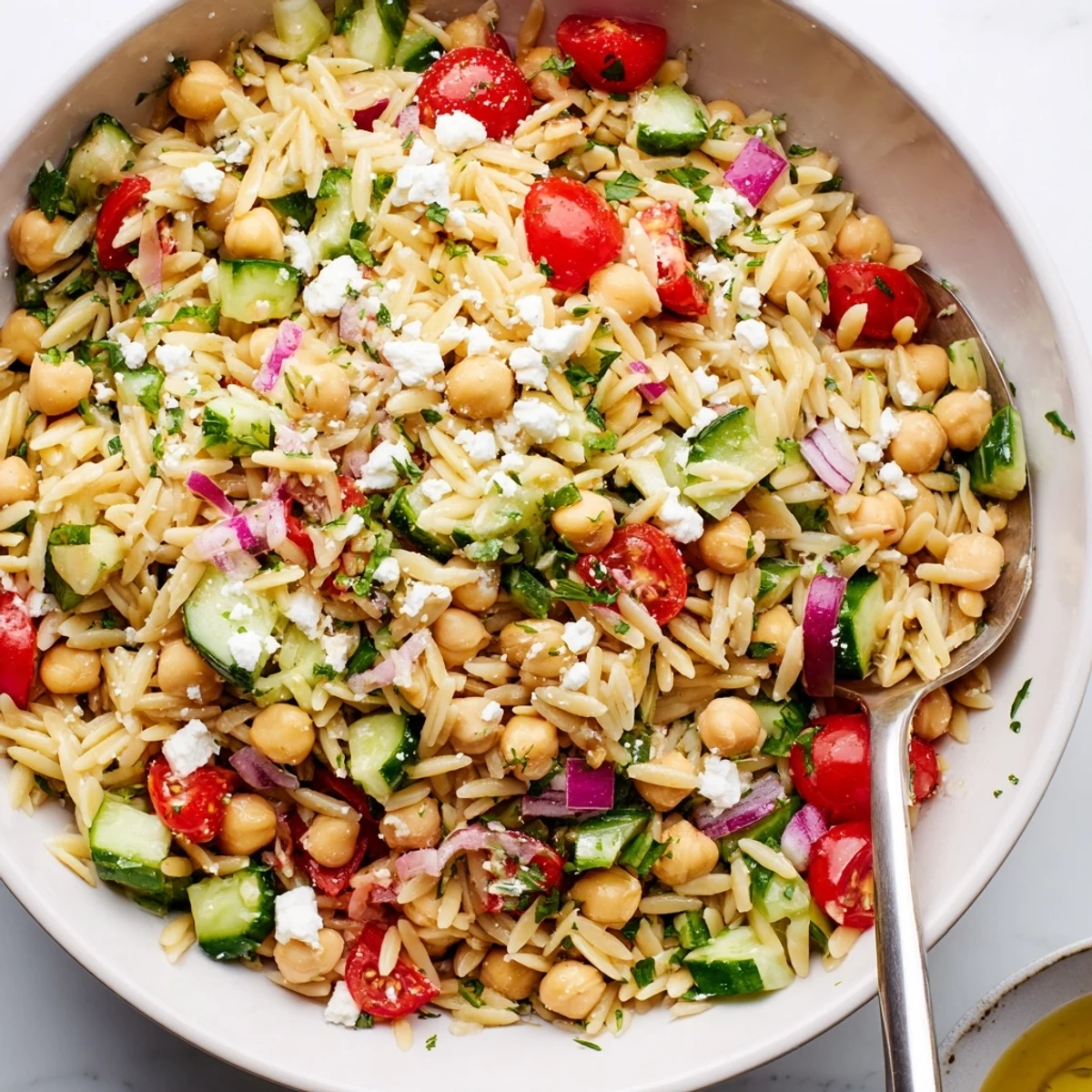 Bright Lemony Chickpea Orzo Salad with crisp cucumber, cherry tomatoes, and fresh herbs, served in a white bowl. 