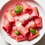A vibrant close-up of Pink Pasta with Beet Cream, the silky sauce glistening with fresh basil and Parmesan.