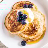 A plate of freshly cooked cottage cheese pancakes, drizzled with sweet maple syrup and topped with berries.