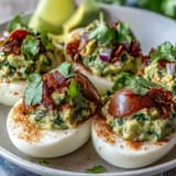 Vibrant deviled eggs filled with rich guacamole, garnished with smoked paprika and fresh cilantro for a zesty snack.  