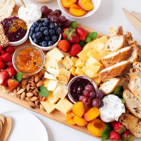 A colorful jam-infused brunch board with cheeses and fresh fruit arrangements.  