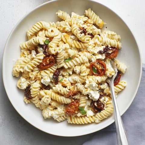 Creamy Baked Feta Pasta with caramelized onions and sun-dried tomatoes in a dish.  