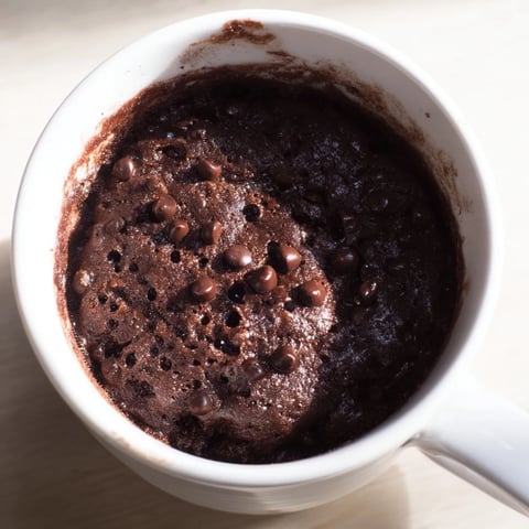 A warm, fluffy Microwaved Mug Cake with melted chocolate chips, ready to devour.