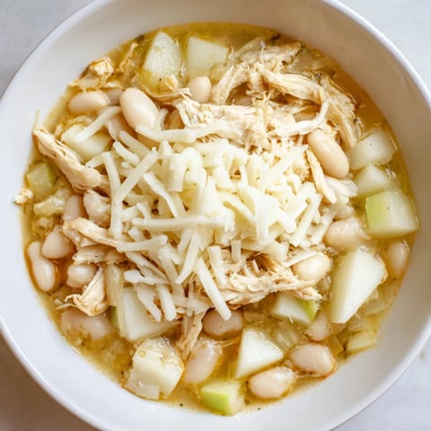 Steaming bowl of 35-Minute White Cheddar Apple Chicken Chili, topped with extra shredded cheddar cheese.