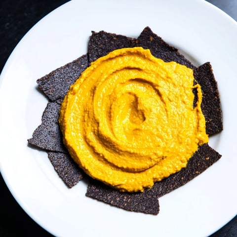 Midnight Sun appetizer: creamy carrot dip encircled by dark charcoal crackers, offering a gourmet experience.