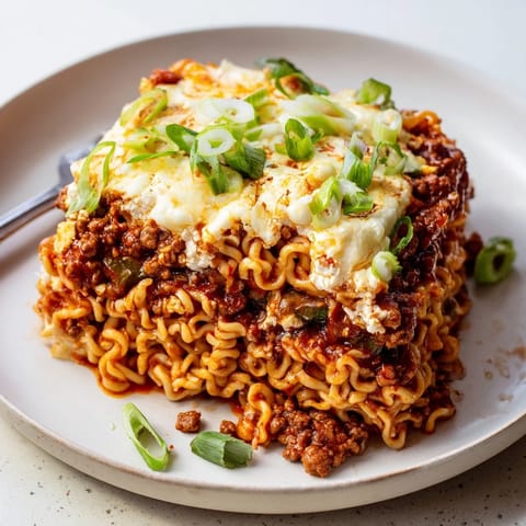 Comforting spicy ramen lasagna baked to golden perfection with fresh green onion garnish.  