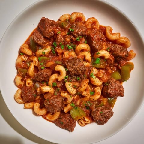 Rich, savory goulash, featuring tender beef, pasta, vibrant tomatoes, and aromatic herbs, served hot.