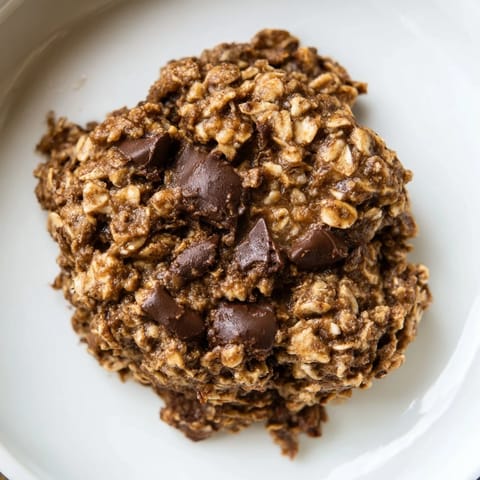 A close-up of a freshly baked chocolate oatmeal breakfast cookie, ready to enjoy with a coffee mug.