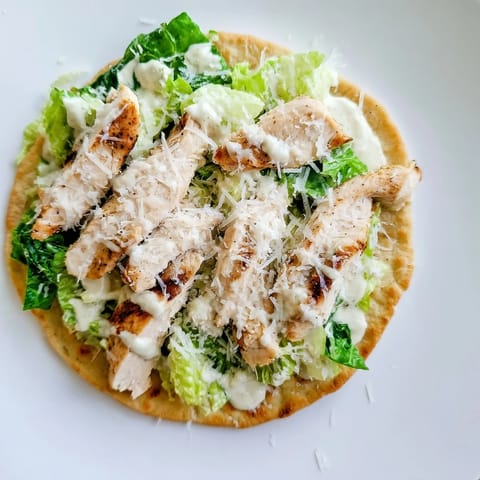 In this Chicken Caesar Flatbread, warm naan is topped with tender grilled chicken, crisp romaine, and shaved parmesan for a satisfying lunch.  
