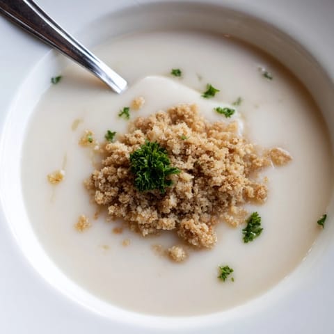 A vibrant, golden bowl of velvety celeriac soup garnished with a generous sprinkle of buttery hazelnut crumble.  