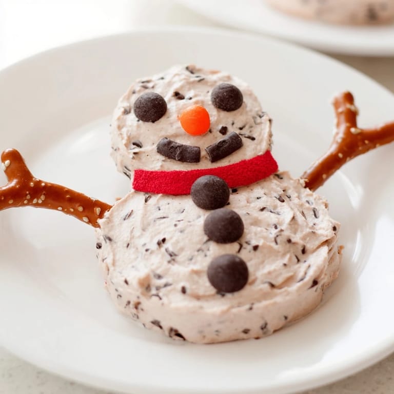 A whimsical Hot Cocoa Dip snowman shape, decorated with pretzels and candy for a holiday dessert.