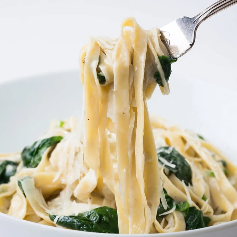 A close-up of Creamy Garlic Spinach Pasta showing steaming fettuccine tossed with fresh spinach and creamy garlic sauce.