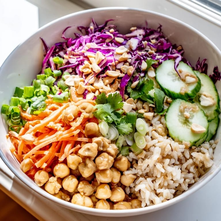 This nourishing Peanut Chickpea Rice Bowl features crunchy peanuts, fresh vegetables, and a zesty peanut sauce, served in a white bowl for a colorful weeknight meal.